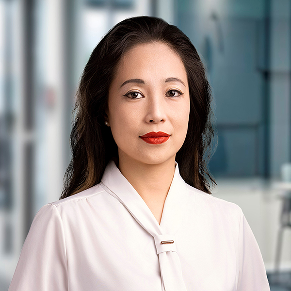 Eine Frau mit langen dunklen Haaren und rotem Lippenstift, die eine weiße Bluse trägt und in einem modernen Büro steht.
