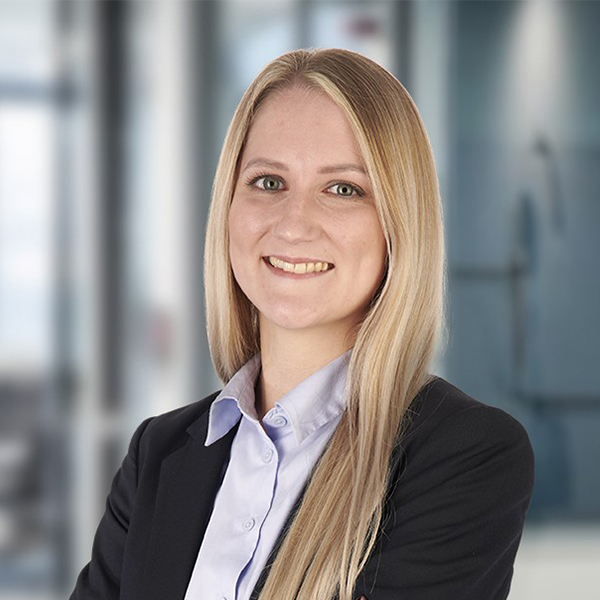 Eine Frau mit langen blonden Haaren im Anzug, die in einer modernen Büroumgebung lächelt.